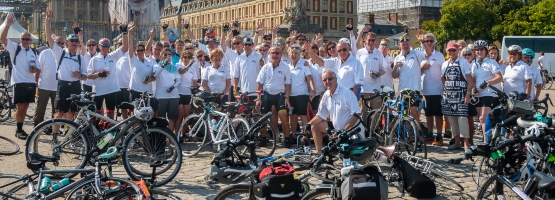 big group of people cheering, all wearing the same white top in front of dozens of bicycles