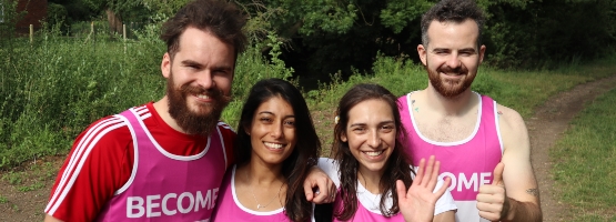 four people smiling and hugging, all wearing Become running vests