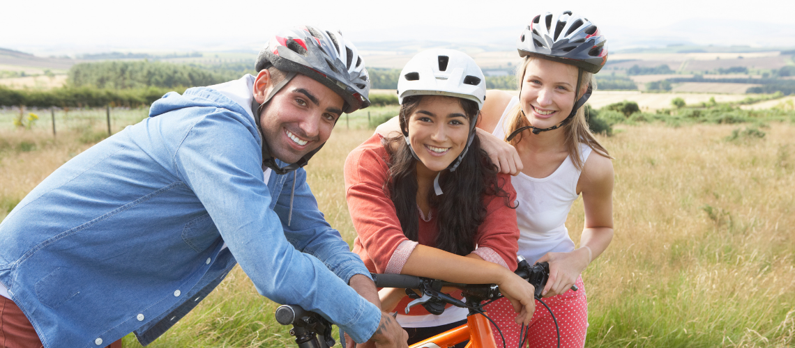 three people smiling and leaning on bicycles wearing cycle helmets